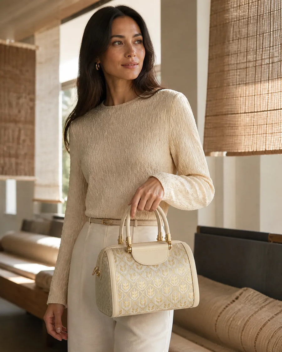 Woman hand carrying an ivory symbolic heritage handbag with wheat motif